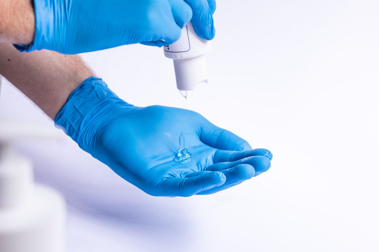 Crop anonymous medic applying antibacterial gel on blue latex gloves on white background in light room in hospital